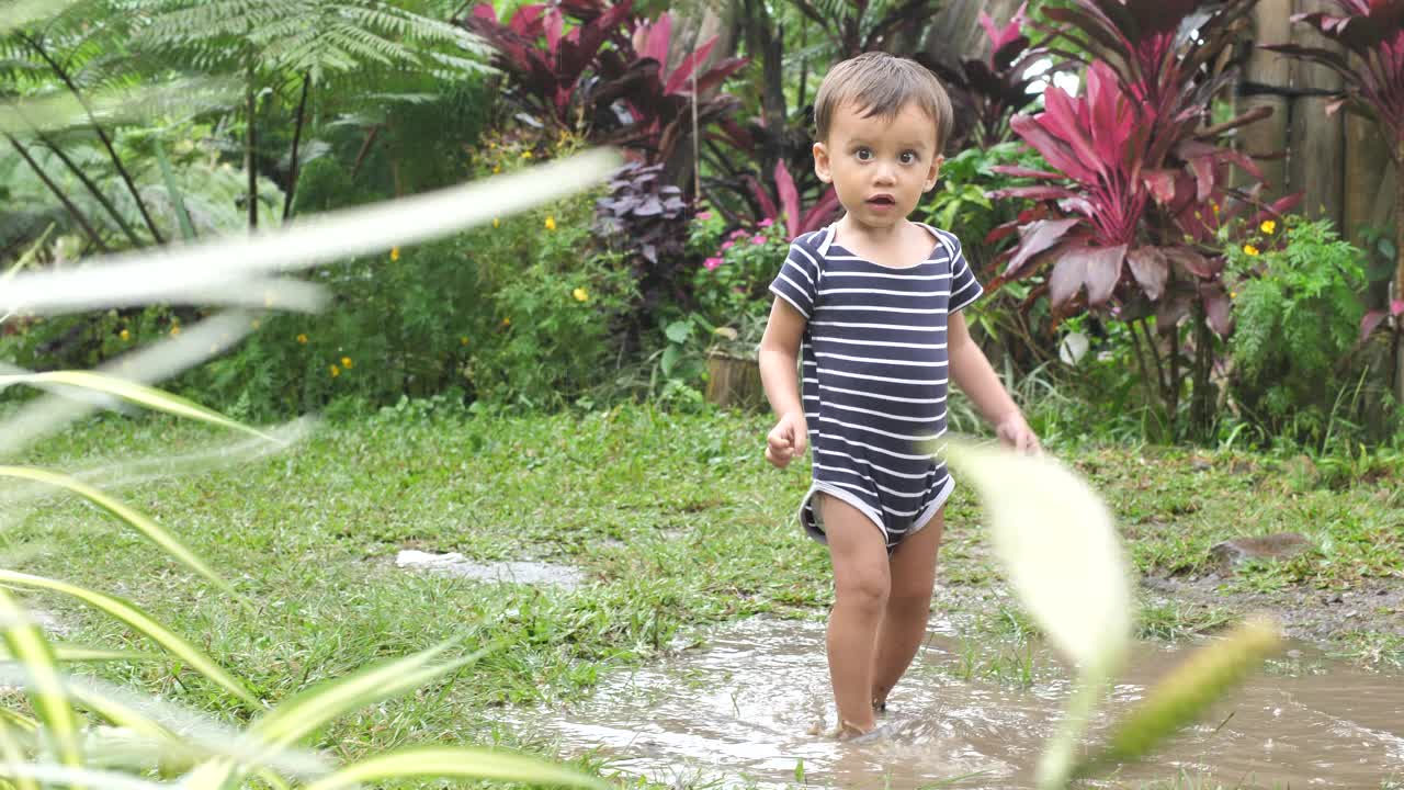 雨后，一个活泼的男孩穿着运动鞋走过院子里的水坑视频素材