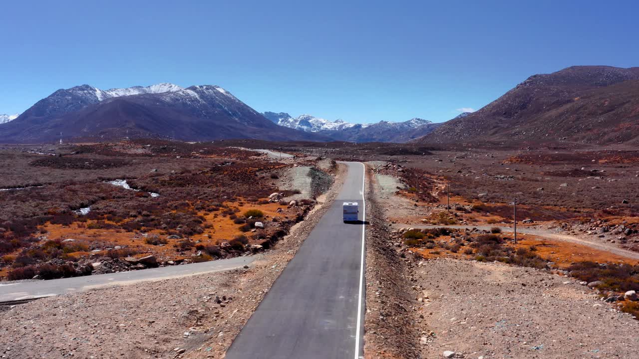 跟随一辆汽车行驶在空旷的道路上，背景是雪山。——空中视频素材