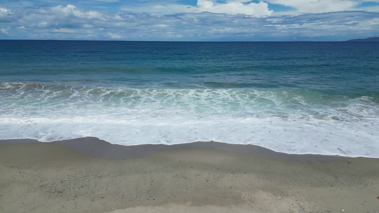 白天，海浪拍打着沙滩，映衬着乌云密布的天空视频素材
