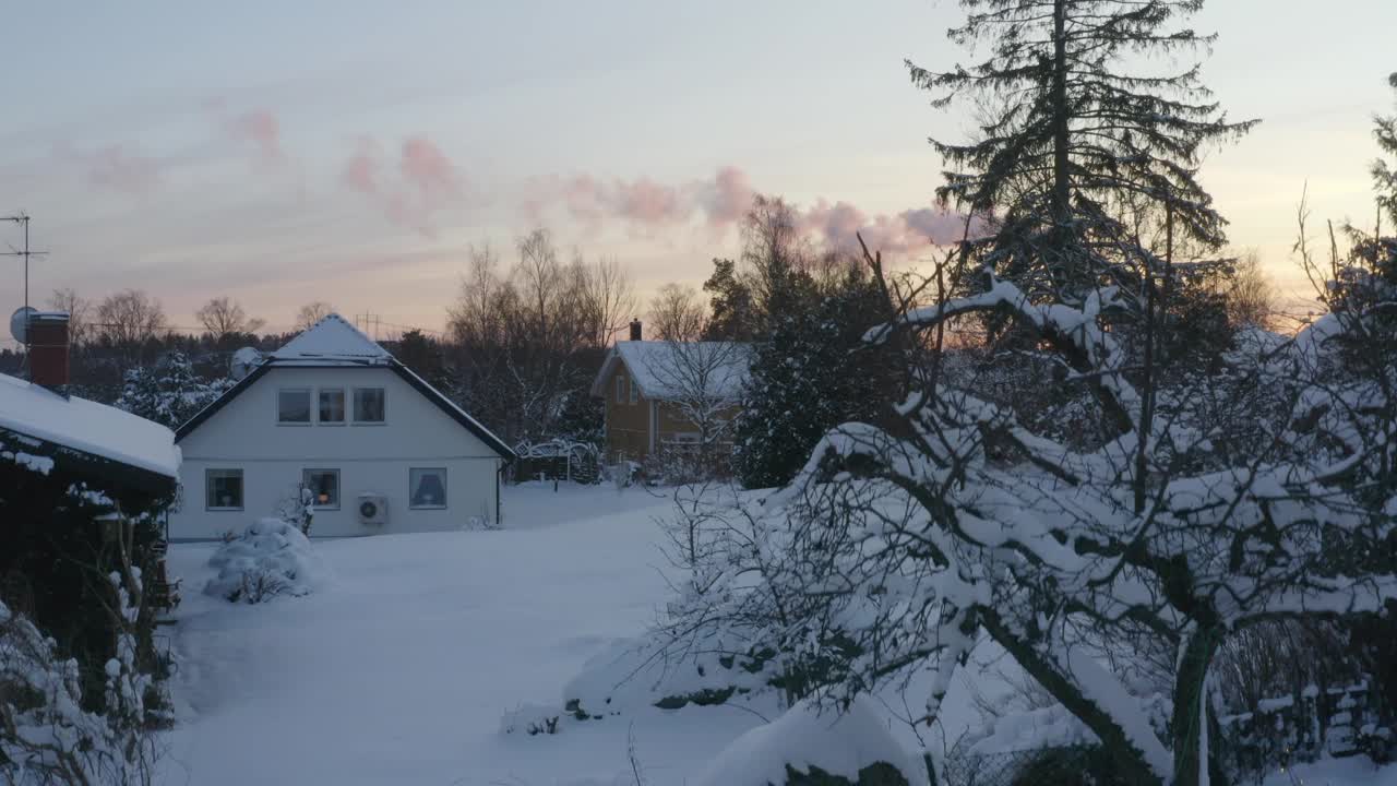 在积雪覆盖的住宅区，从无人机上看到的区域供热厂烟雾与冬季日落的映衬视频下载