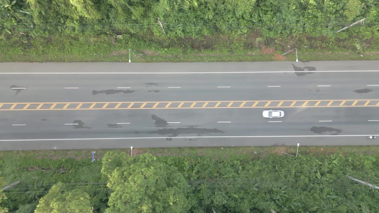 视频显示，一架无人机从右向左缓慢飞行，拍摄了一条宽阔的道路，周围是茂密的森林，汽车行驶平稳。视频素材