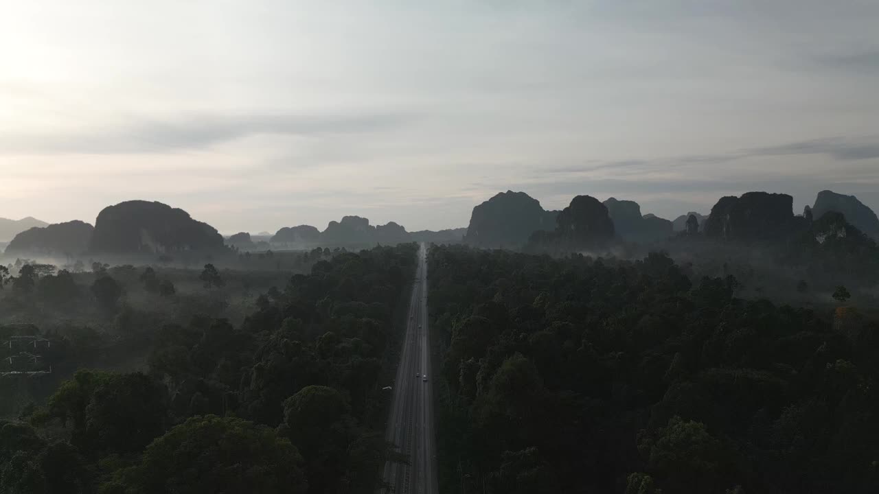 一架无人机在一条长长的直路上缓慢飞行，早上汽车来回行驶，逐渐上升，直到远处的森林、山脉和雾视频下载