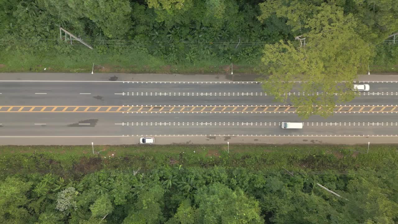 视频显示，一架无人机从右向左缓慢飞行，拍摄了一条宽阔的道路，周围是茂密的森林，汽车行驶平稳。视频素材