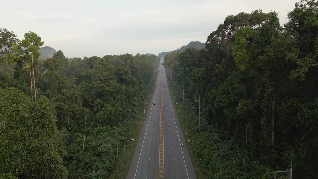 一架无人机从一条长长的直路上缓慢飞行，早晨汽车来回行驶，逐渐上升，直到清晨看到远处的森林、山脉和薄雾视频素材