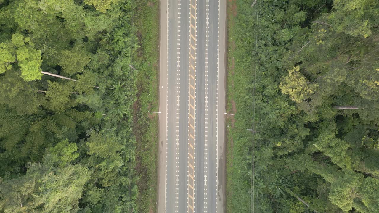 视频显示，一架无人机缓慢地从底部飞到顶部，拍摄了一条宽阔的道路，周围是茂密的森林，汽车行驶平稳。视频下载