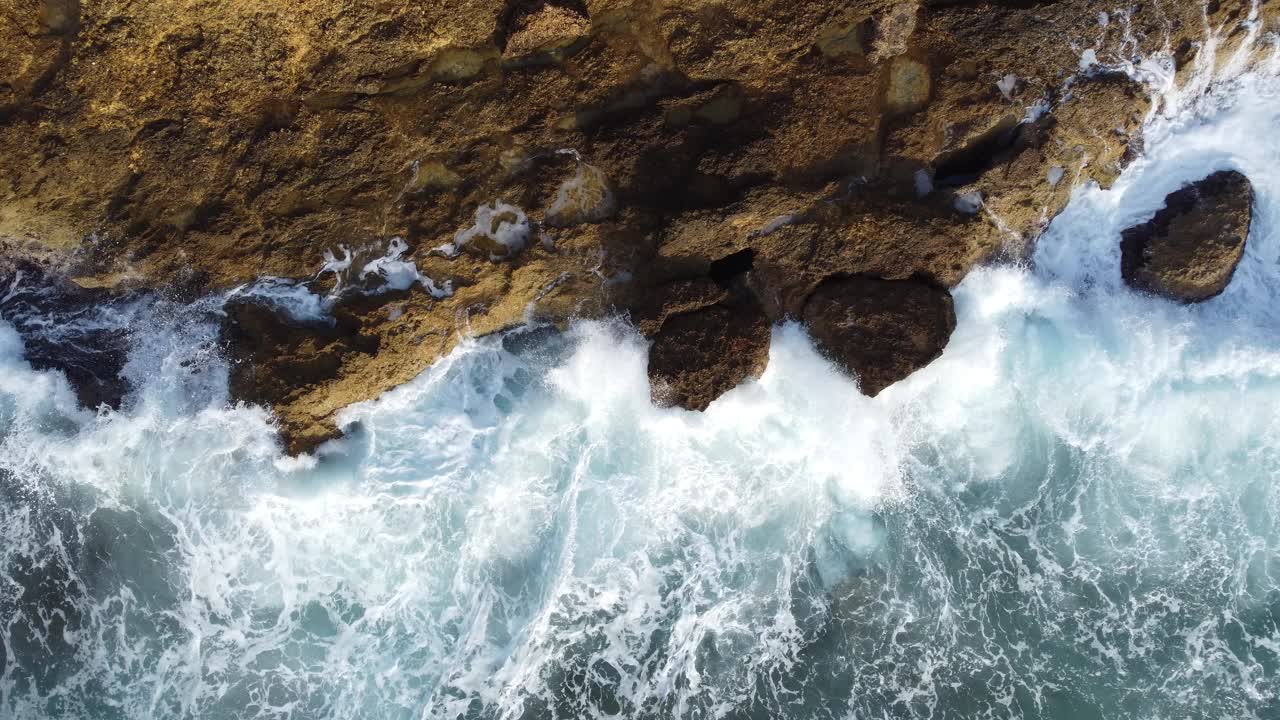 从上往下看，强大的海浪冲击着岩石海岸。海浪冲击着海边的岩石。视频下载