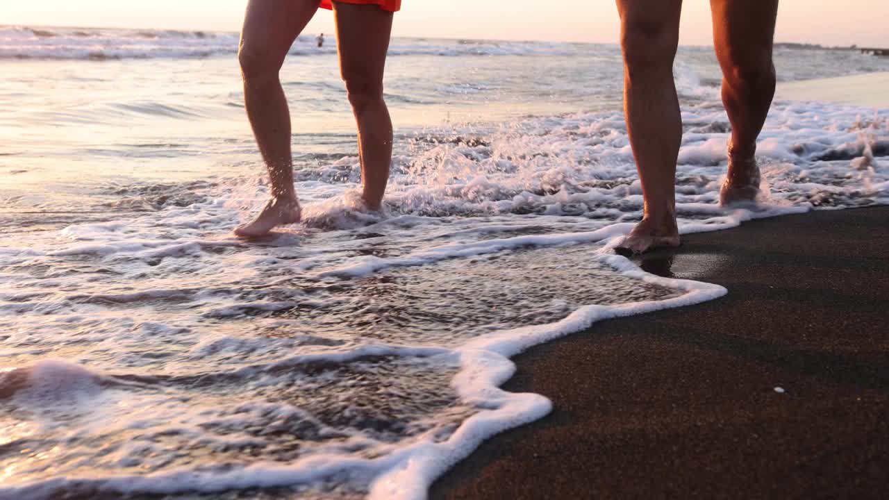 一对夫妇的腿在黑暗的沙滩上沿着海浪散步视频素材