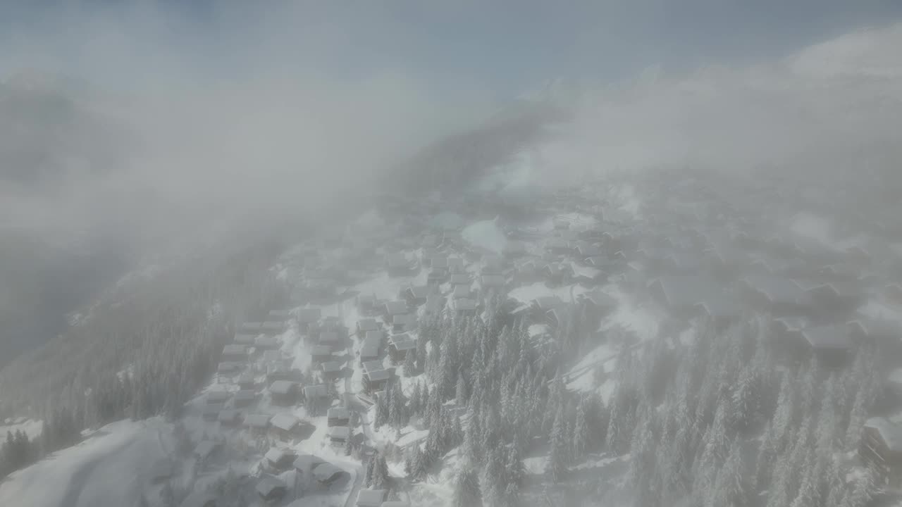 无人机在冬天穿过云层飞行。背景是一个雪中的村庄。瑞士的Bettmeralp视频素材