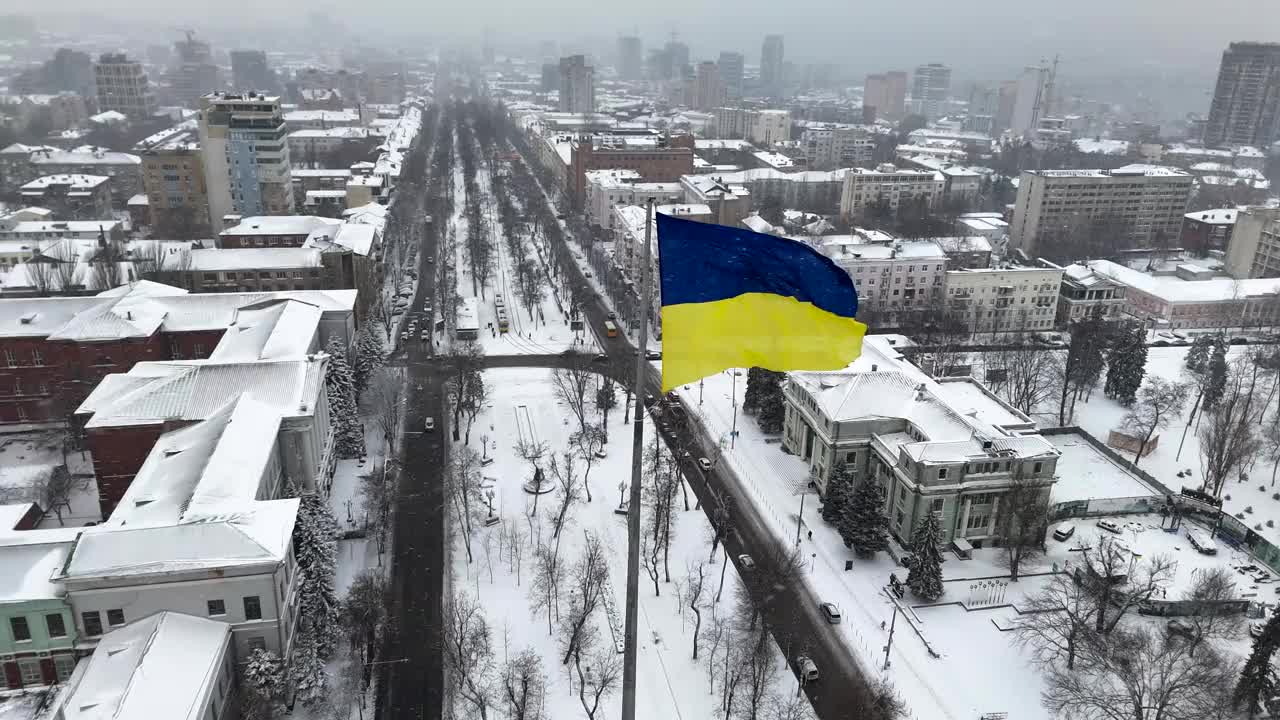 迎风飘扬的乌克兰国旗，背景是冬天的第聂伯罗市和白雪皑皑的街道鸟瞰图。视频素材