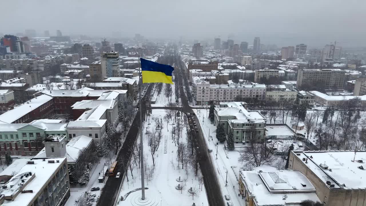 迎风飘扬的乌克兰国旗，背景是冬天的第聂伯罗市和白雪皑皑的街道鸟瞰图。视频素材