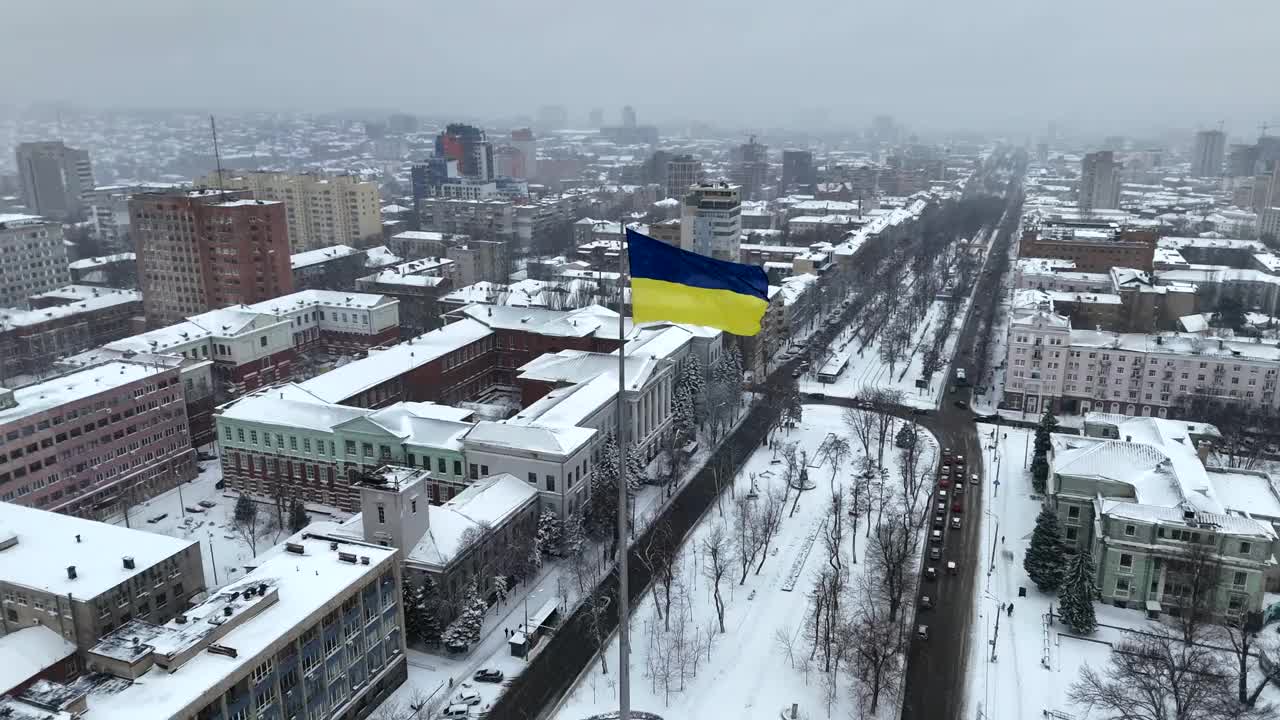 迎风飘扬的乌克兰国旗，背景是冬天的第聂伯罗市和白雪皑皑的街道鸟瞰图。视频素材