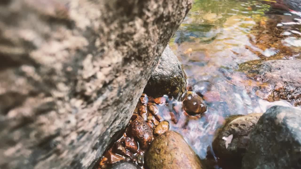 夏天，绿色的森林里水流湍急。一条小瀑布从岩石下面冒了出来。用慢动作拍照视频素材