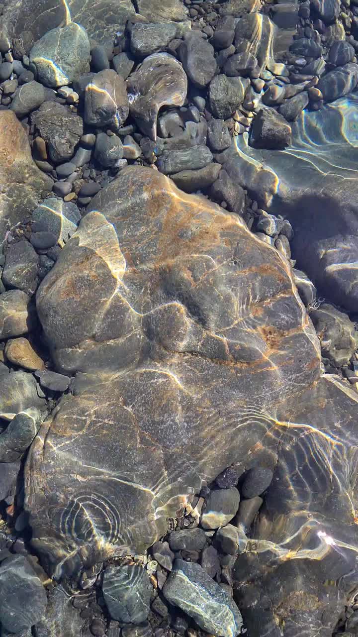 透明的海水，海底有大块的石头，阳光刺眼，水面泛起涟漪，背景清晰可见。视频素材