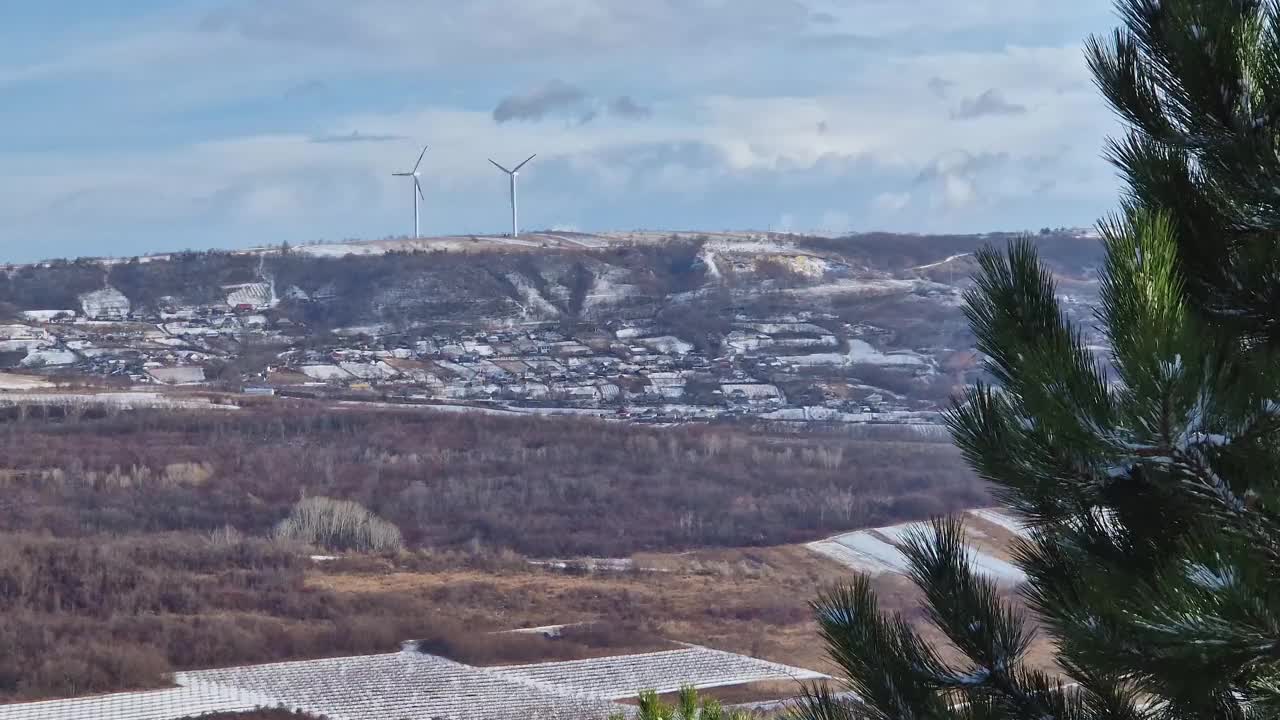 摩尔多瓦的乡村山谷里有许多小村庄，在白雪覆盖的小山顶上，风力涡轮机在旋转视频素材