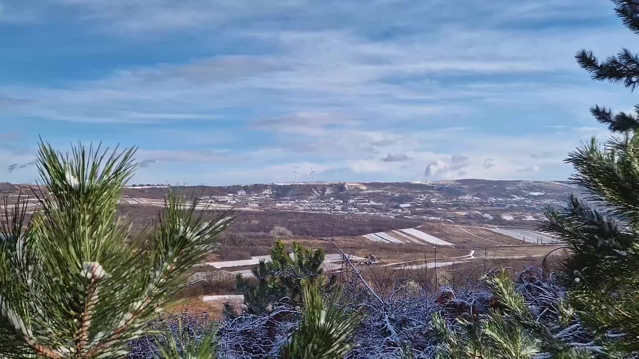 摩尔多瓦的乡村山谷里有许多小村庄，在白雪覆盖的小山顶上，风力涡轮机在旋转视频素材