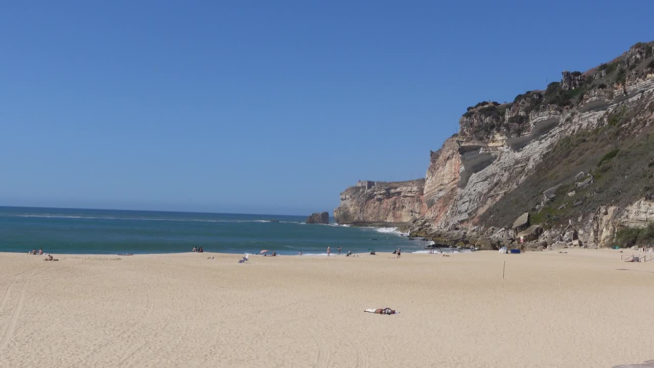 沙滩纳扎雷海滩(普拉亚达纳扎雷)与岩石悬崖的背景在纳扎雷，葡萄牙视频素材