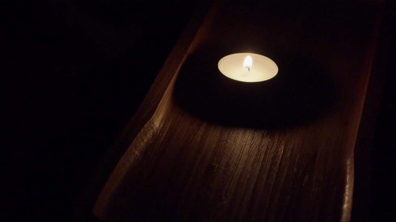 浓黑的房间里，单支茶烛在浓黑的棕色木盘里燃烧视频素材