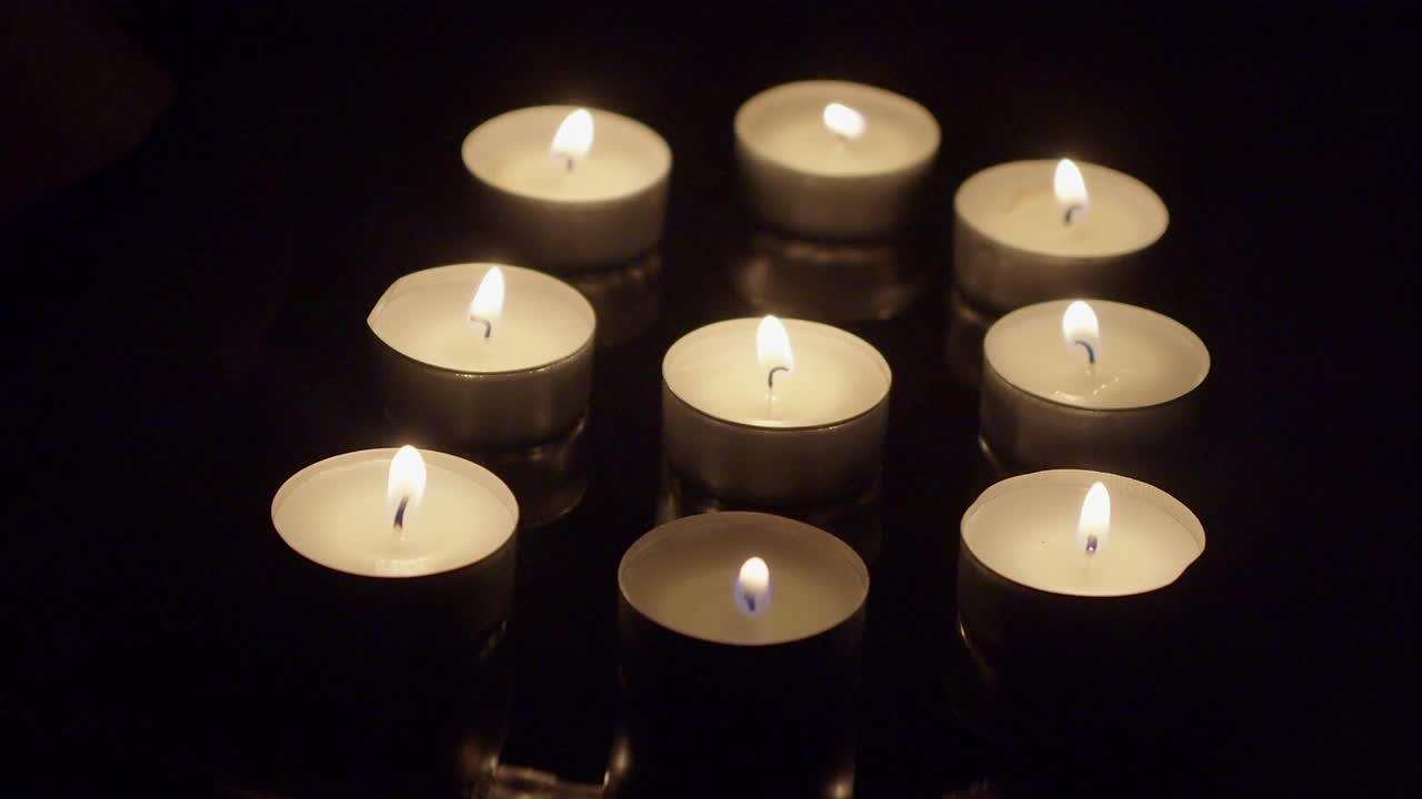 一组燃烧的茶蜡烛在反射托盘吹灭了黑暗视频素材