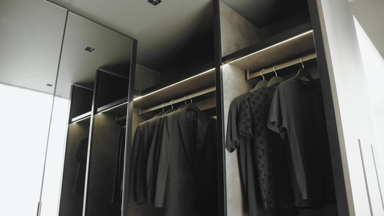 衣柜的特写与衣架黑色t恤和黑色夹克。男人的衣橱。更衣室有背光，慢动作视频素材