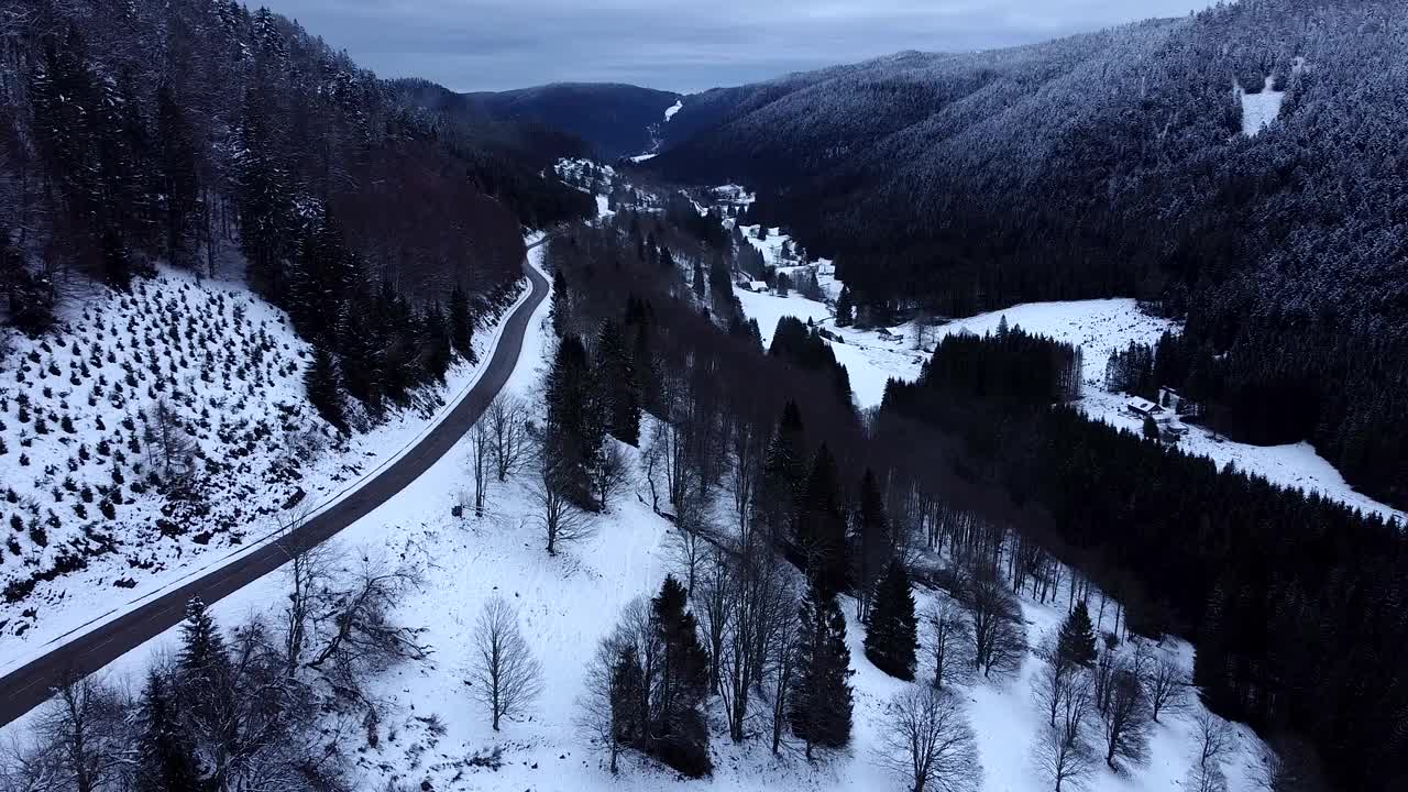 空中低空飞行的山路与积雪覆盖的森林在冬季在上孚日，法国视频素材