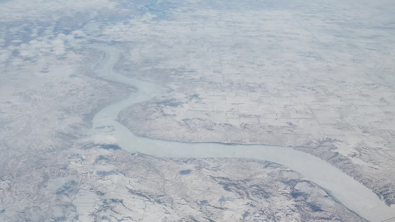 冬季在北美上空飞行。飞机窗外的风景。冰冻的河流和平原上的积雪视频下载