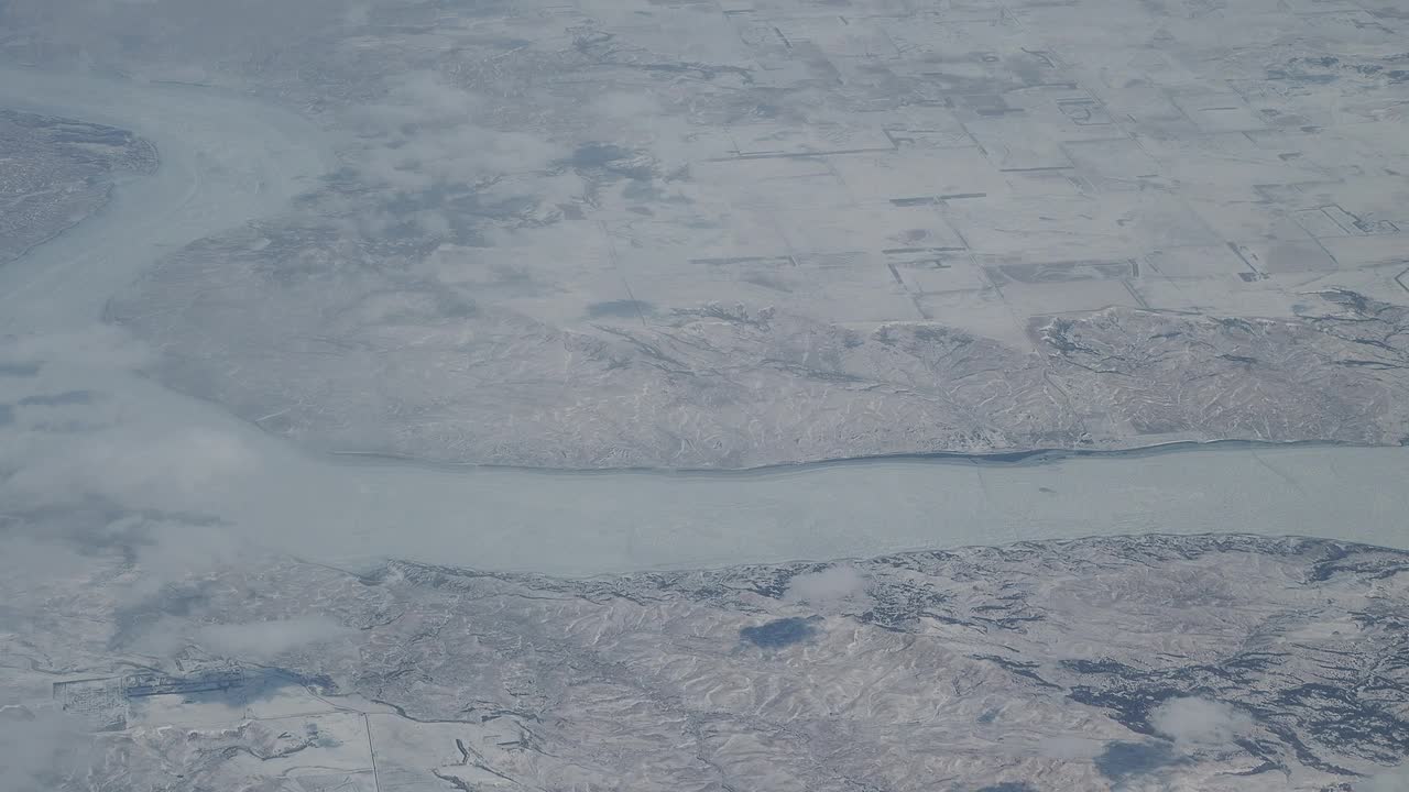 冬季在北美上空飞行。飞机窗外的风景。冰冻的河流和平原上的积雪视频素材