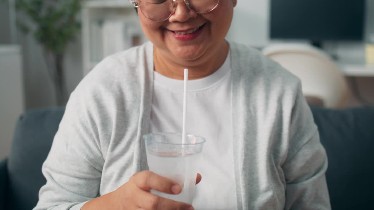 紧张的亚洲老年妇女坐在家里的沙发上抚摸着牙齿问题的脸颊、牙齿敏感的不快乐的祖母、牙齿疼痛的老年妇女视频下载