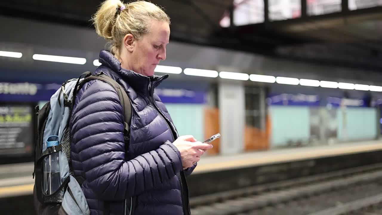 一名女子一边等火车，一边用智能手机发短信。视频素材