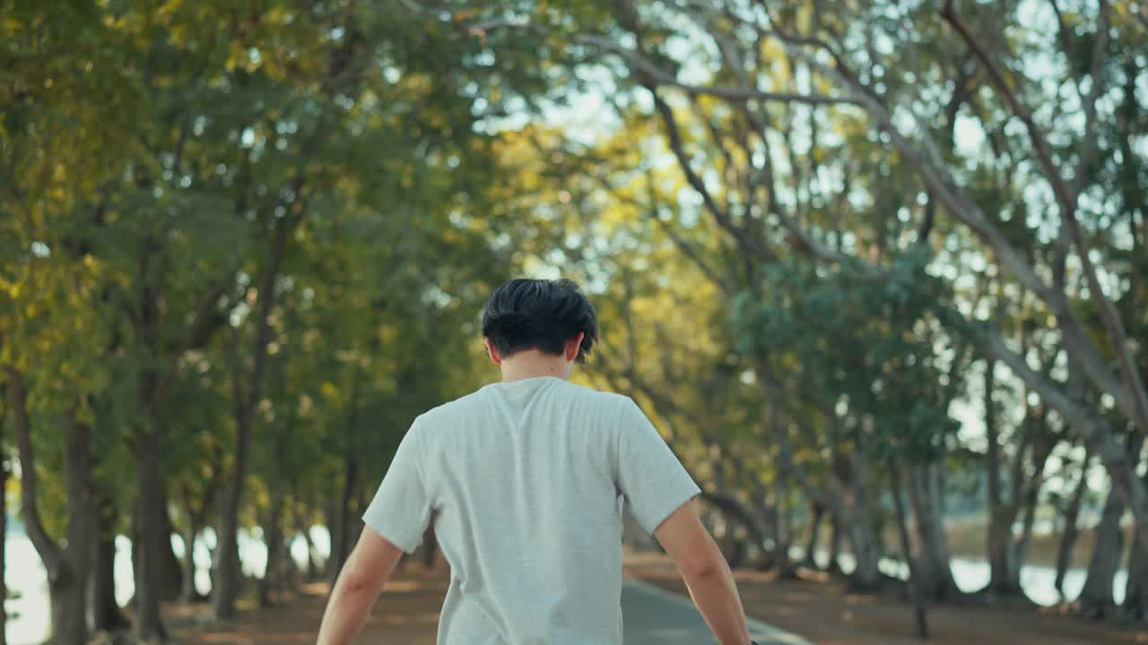 有吸引力的亚洲男子慢跑在公园的树与阳光的背景，健身男子跑步，训练跑步锻炼。视频素材