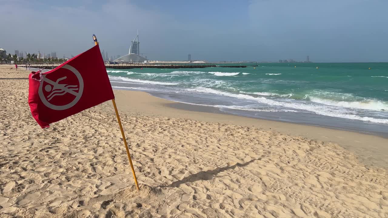 在阿联酋迪拜的海滩上，一面红色的警告旗迎风飘扬。海上有风暴，不能游泳。红旗作为警告标志视频素材