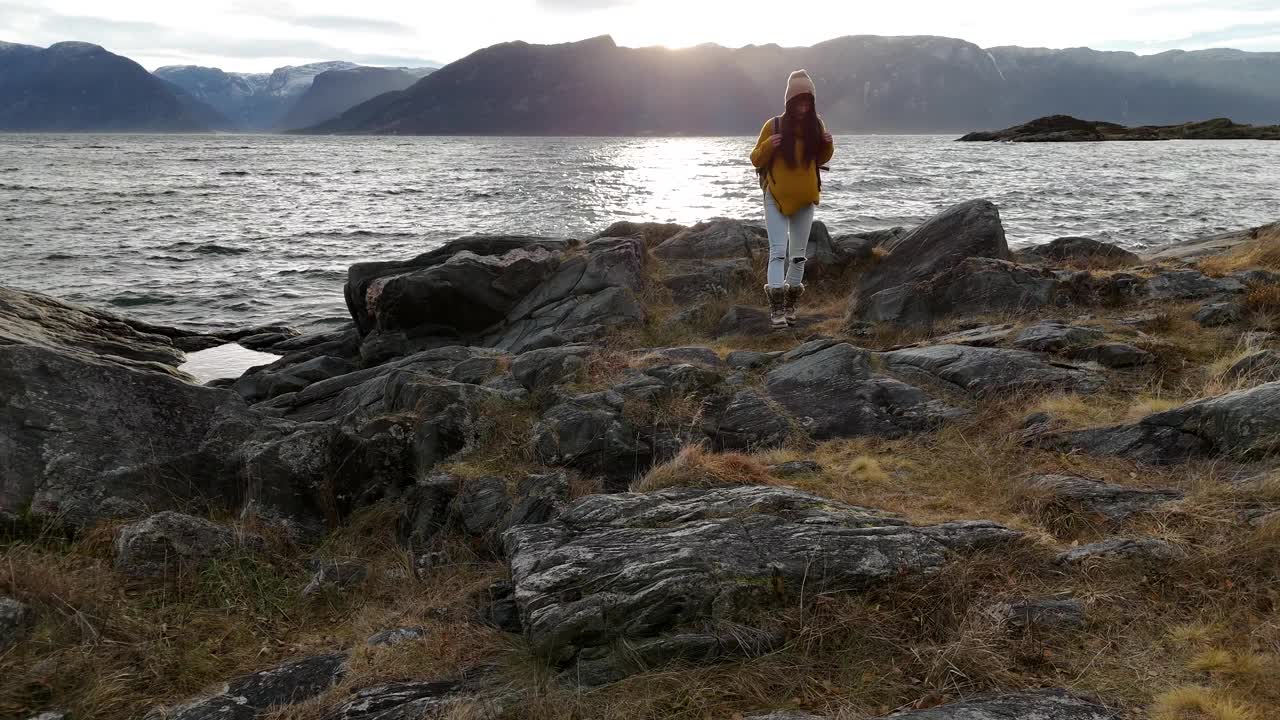 冒险的女人在日出时沿着海岸散步，视频记录与峡湾背景无人机-冒险和赋权的概念视频素材