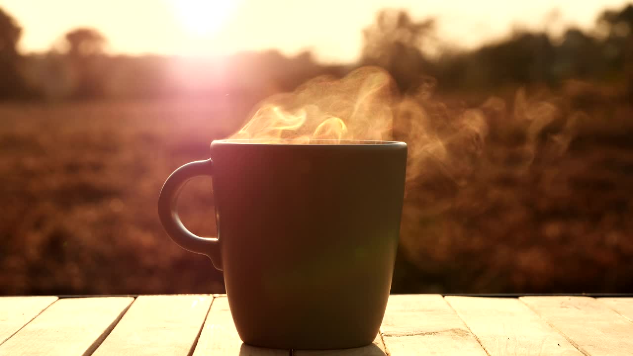 热咖啡杯，咖啡杯中有美丽的蒸汽烟雾的杯子，放在桌子上，早晨的阳光自然户外背景，4K。概念热咖啡，茶，食品，饮料，浓缩咖啡，早餐视频下载