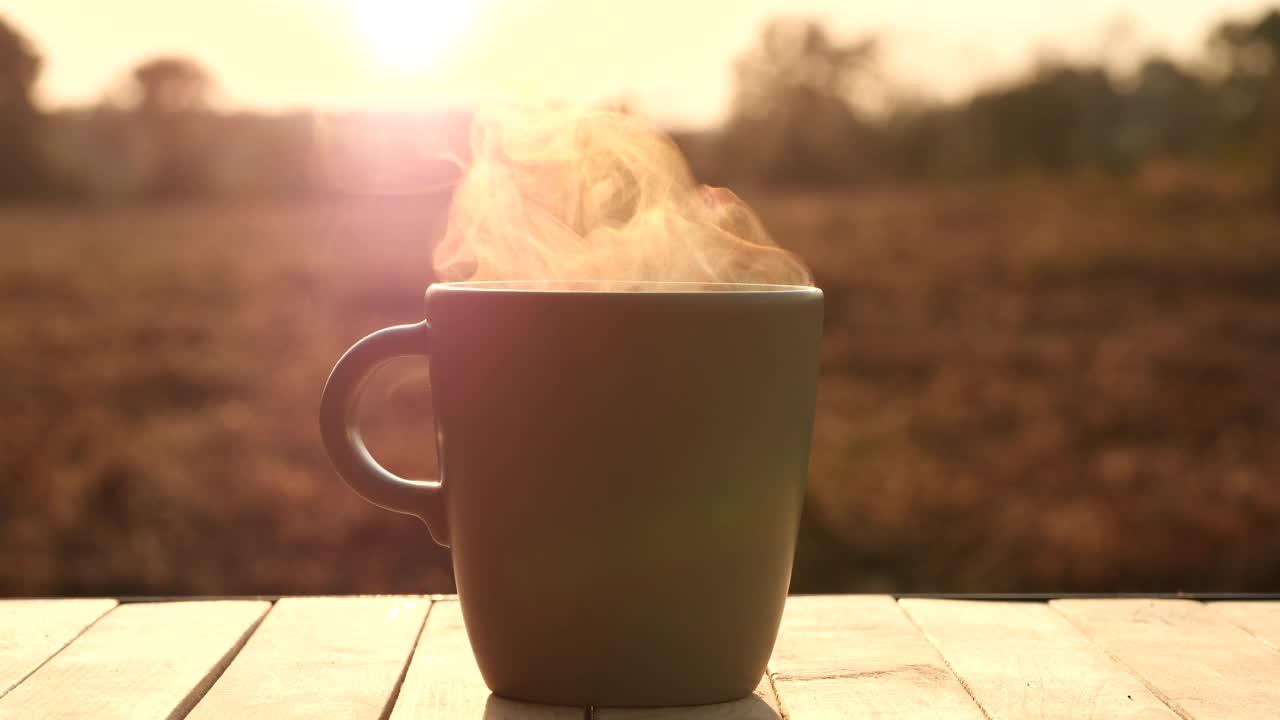 热咖啡杯，咖啡杯中有美丽的蒸汽烟雾的杯子，放在桌子上，早晨的阳光自然户外背景，4K。概念热咖啡，茶，食品，饮料，浓缩咖啡，早餐视频下载