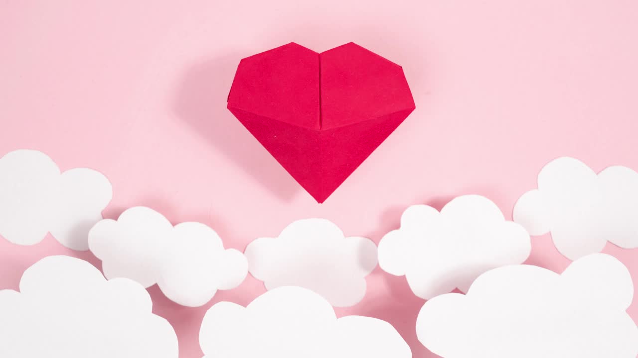 体积折纸心在白云间摇曳飞舞。贺卡。粉红色的背景。爱的象征。视频下载