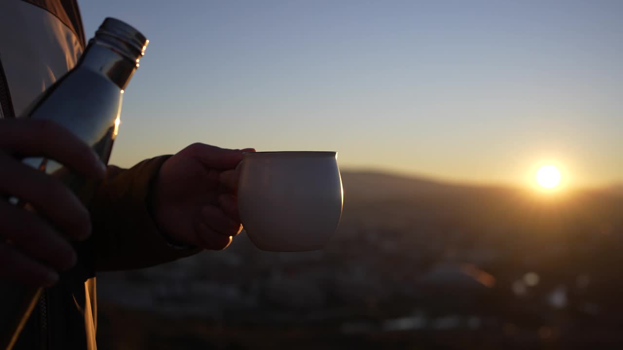 男子的手从旅行热水瓶中倒出热饮。日落的背景。视频素材