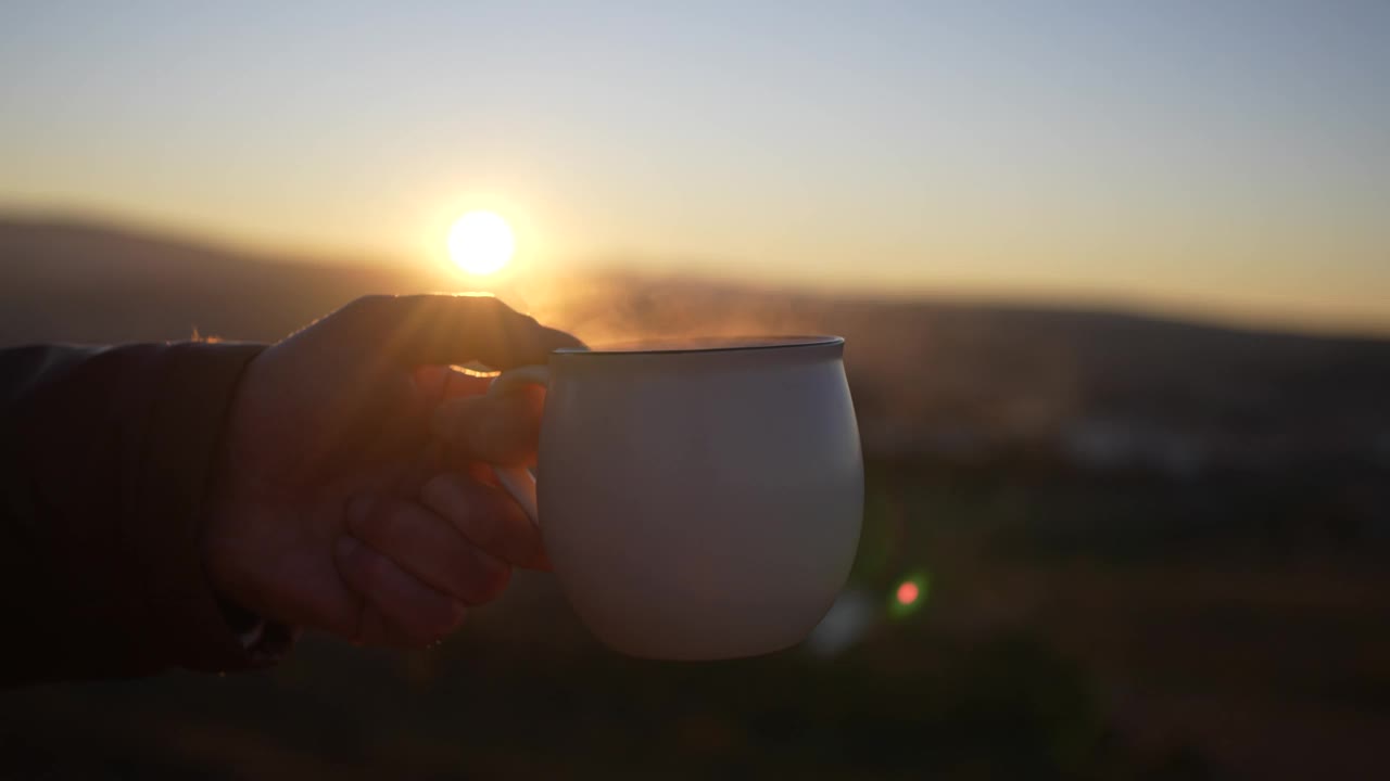 手持杯热饮夕阳背景。视频素材