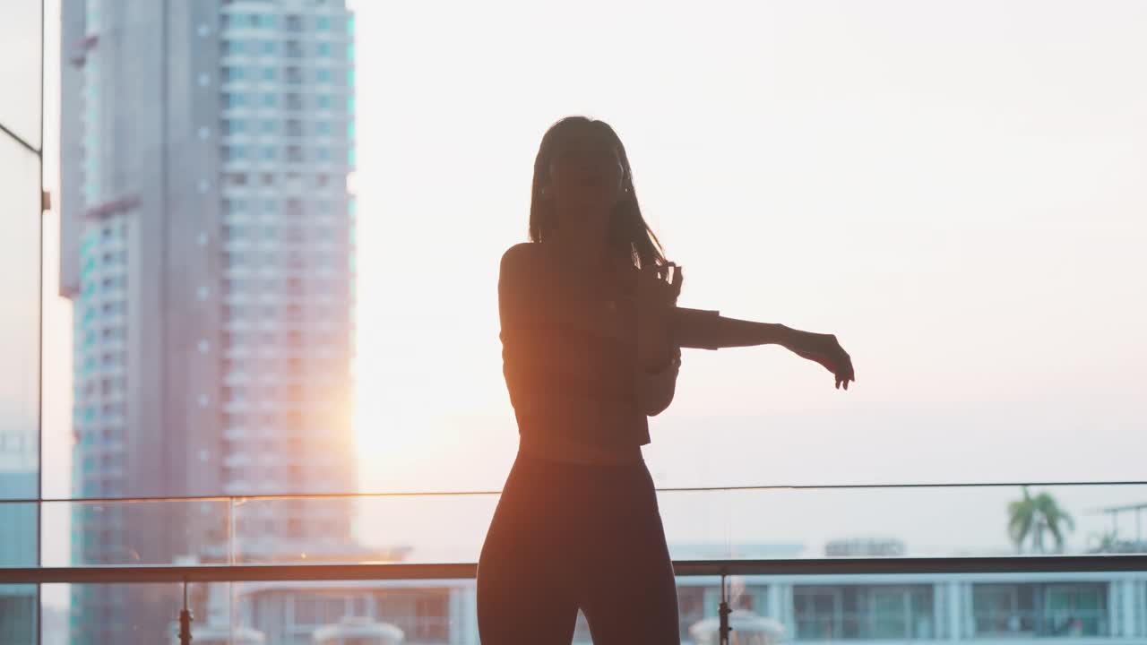 健康的亚洲年轻女性在晨曦前的户外运动前热身伸展双臂，享受自然的晨光，愉悦的女性在都市环境中进行锻炼活动视频素材