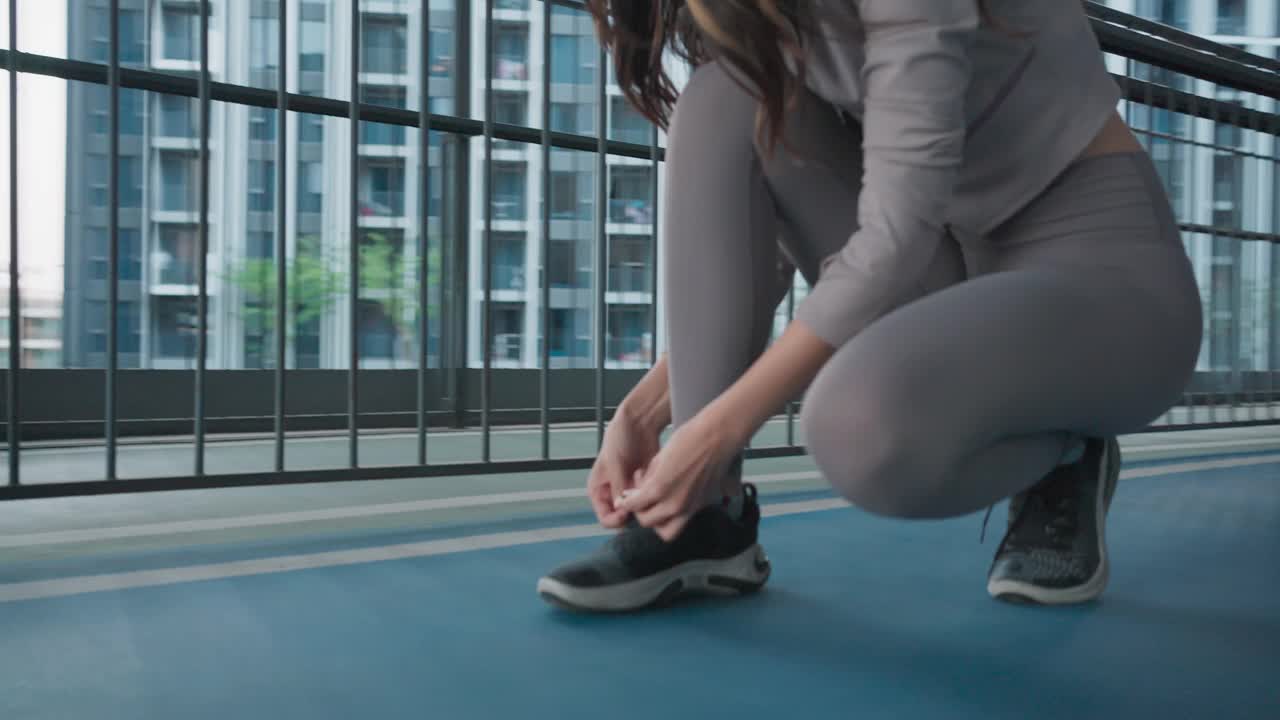 运动的亚洲年轻女子在慢跑前系鞋带，在城市高楼的公共跑道上跑步，积极的生活方式与锻炼活动视频素材