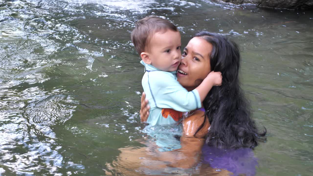 年轻的母亲带着小儿子在清澈的河水中游泳视频素材