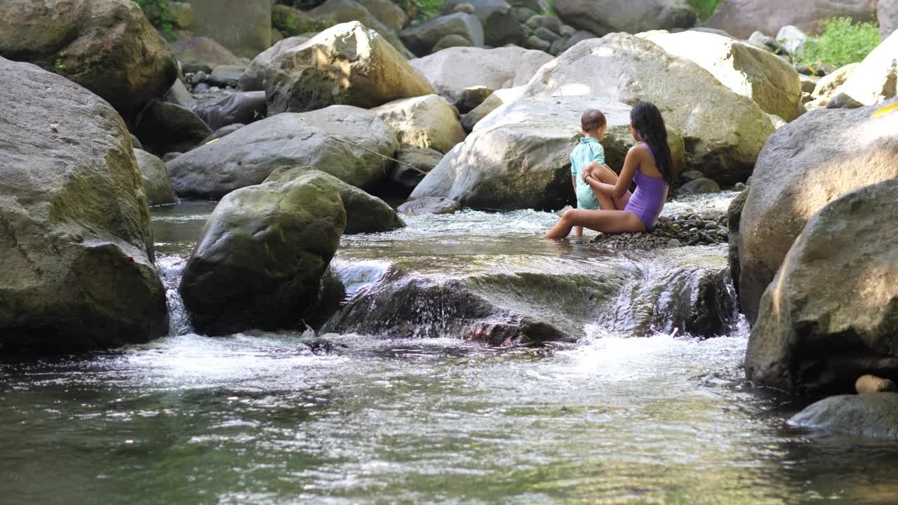 年轻女子带着小孩在岩石河的激流中洗澡视频素材