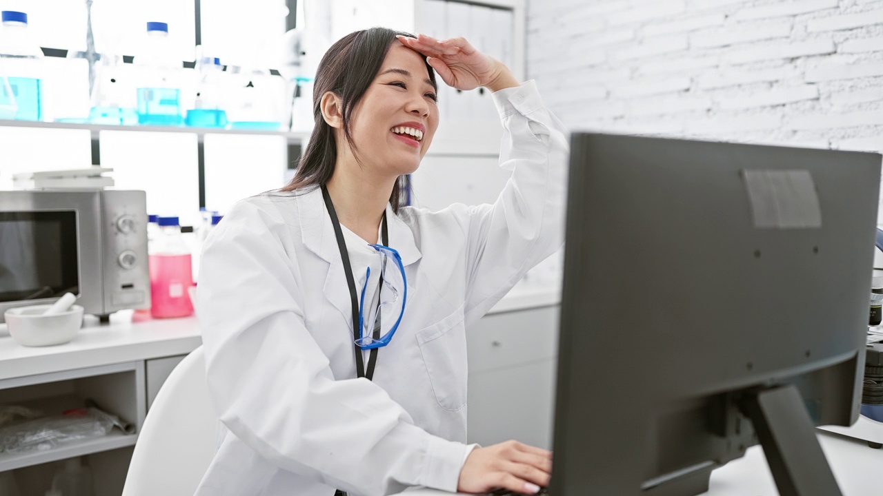 Young chinese scientist woman's happy gaze far away as hand aids her search in lab视频素材