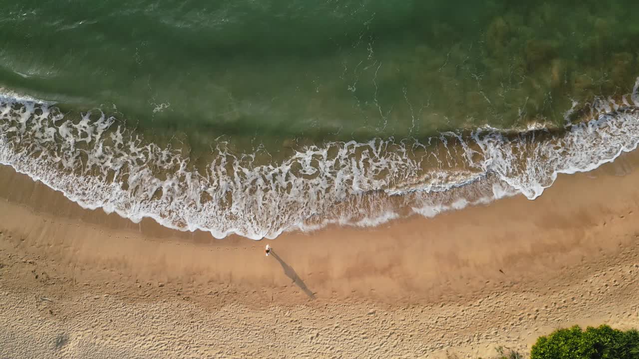 鸟瞰图，孤独的雌性漫步在沙滩上，海浪轻轻地拍打着海滩。轻松漫步大自然，宁静理念，休闲旅游视频，养生静修内容。视频素材