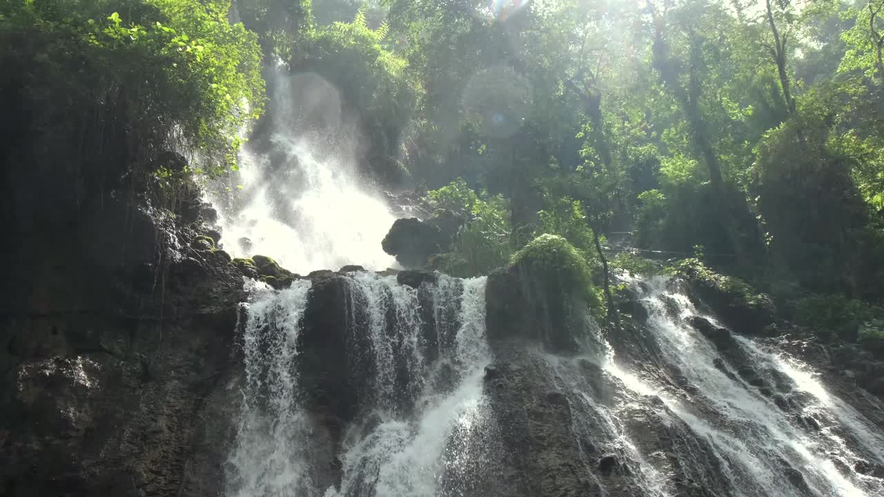 瀑布的水在阳光照射下在山岩峭壁上快速流动视频下载