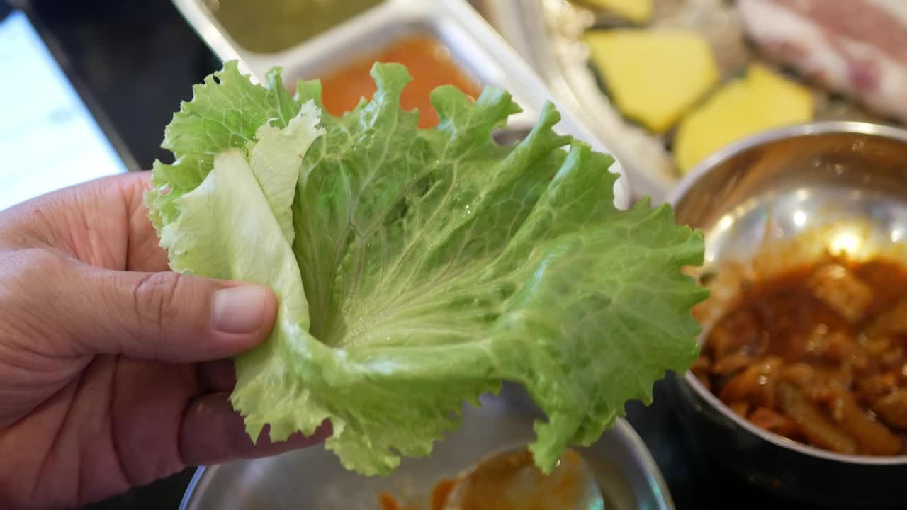 同时用筷子挑出猪肉，在韩国传统的炭锅炉中烤熟后放入蔬菜中食用视频素材