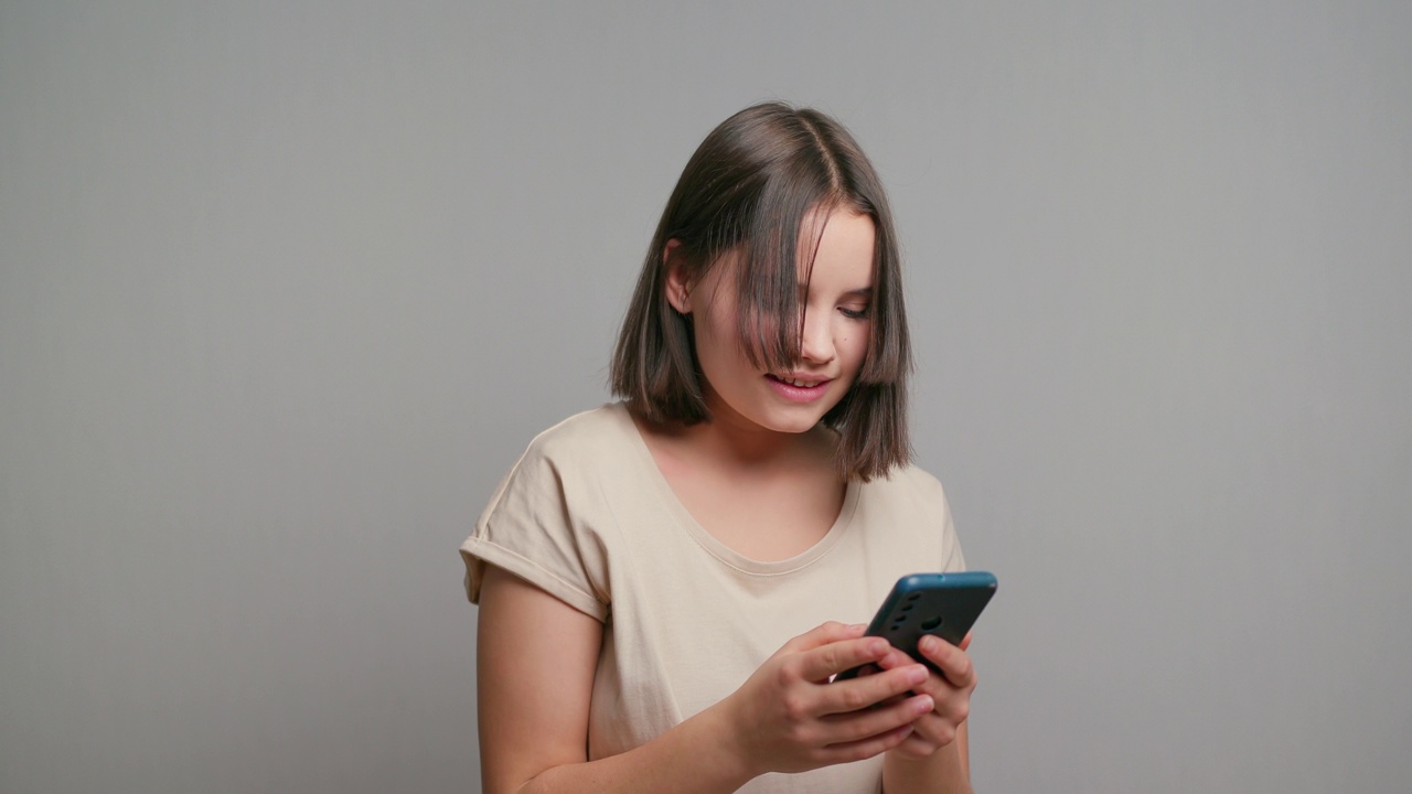 微笑的拉丁少女使用手机智能手机在灰色背景的工作室视频素材