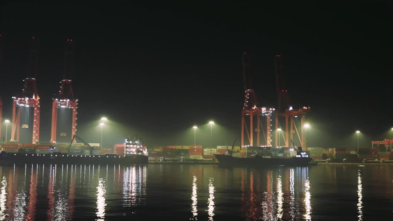 夜港里被照亮的起重机的剪影，倒映在水中。雄伟的夜景与点亮的集装箱起重机轮廓，宁静的水面反射。繁忙的港口，夜间作业需要多台起重机视频素材