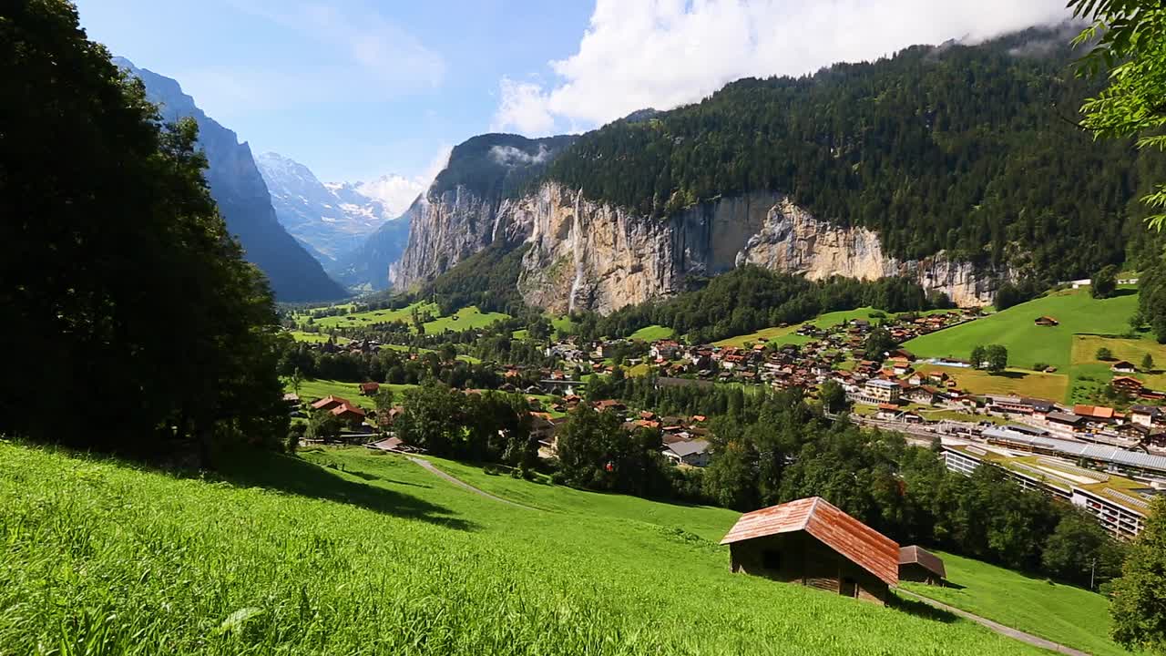 在一个阳光明媚的日子里，看到高山清新的绿色草地。Lauterbrunnen valley, Staubbach瀑布，欧洲。视频下载