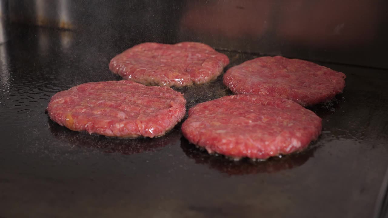 四个汉堡肉饼在餐厅厨房的热炉子上煎的特写。视频素材