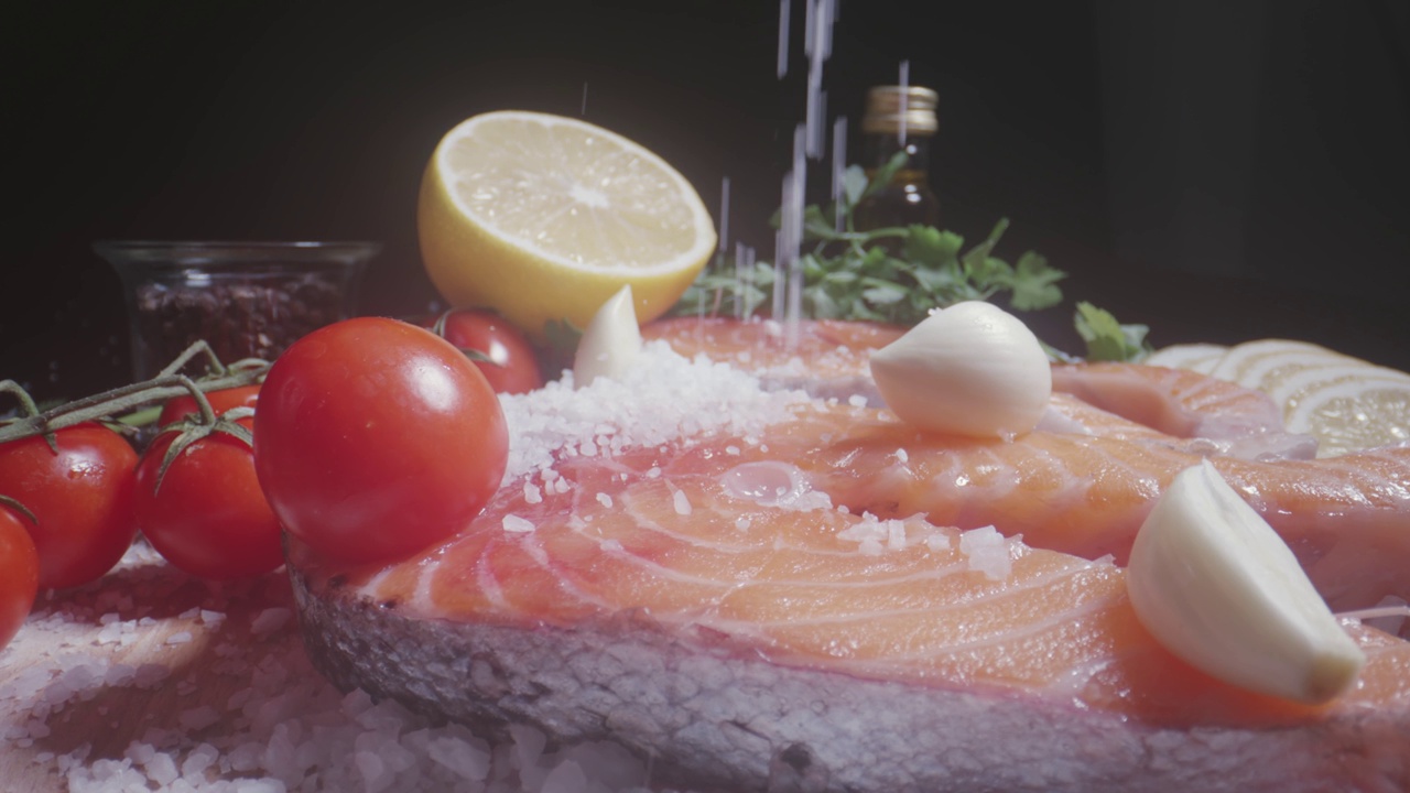 用慢动作将盐浇在新鲜的鱼排、生鲑鱼片、柠檬和香料上视频素材