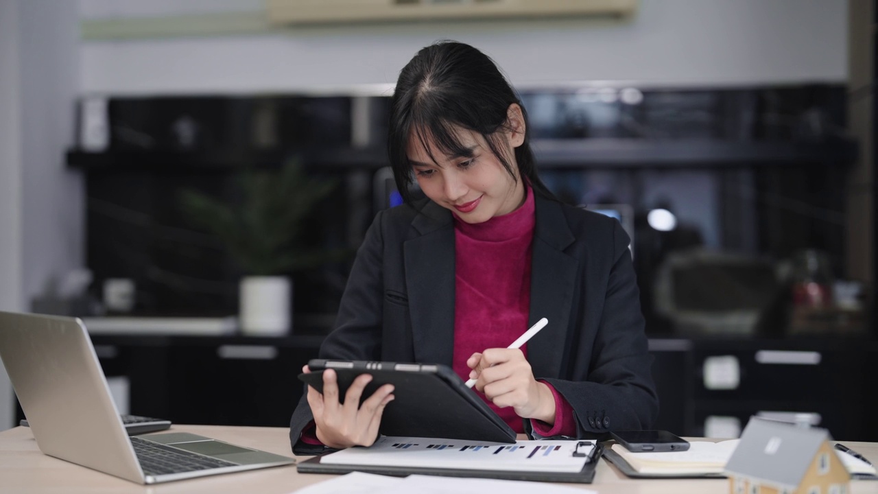 自信的亚洲女商人积极地在她的平板电脑上计划和输入她的商业项目，专注于她现代办公风格的工作桌旁视频素材